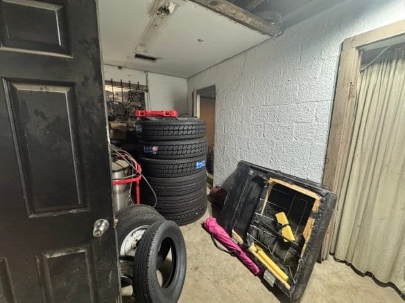 Industrial storage space featuring tires, tools, and equipment on a concrete floor with a white brick wall and curtain backdrop.