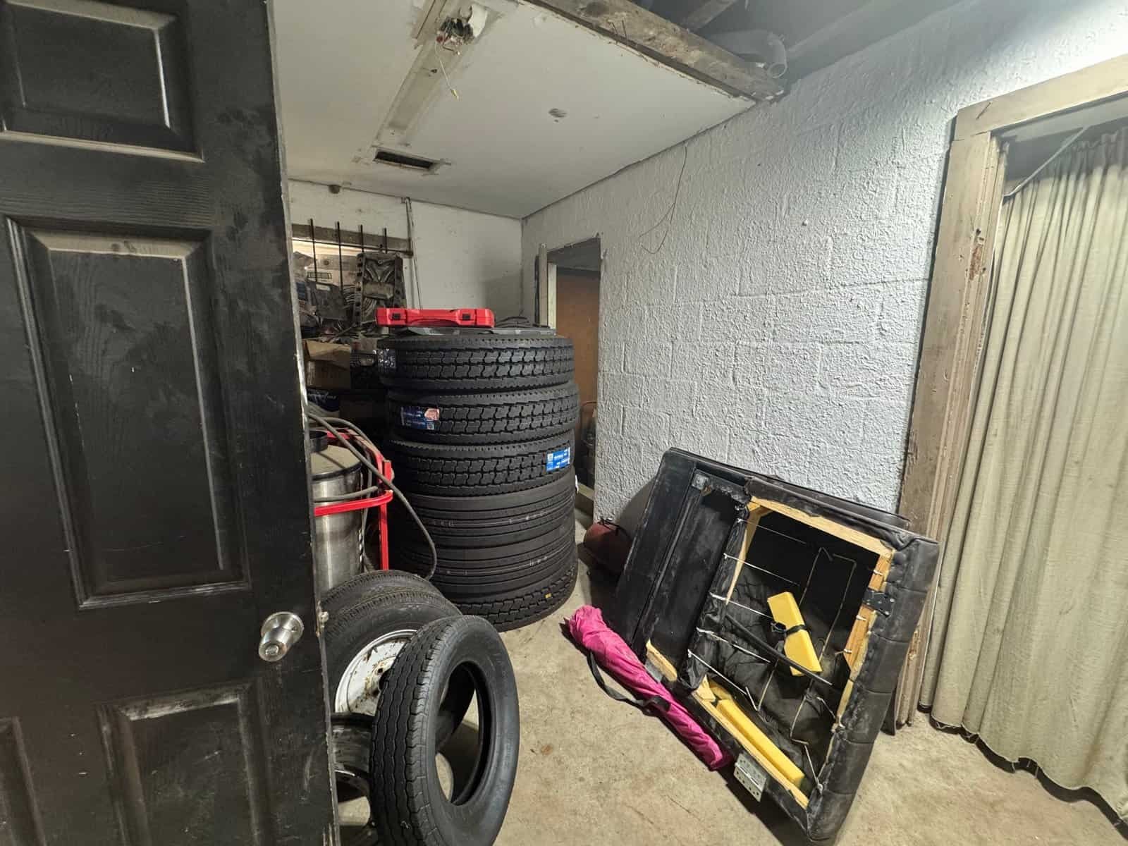 Industrial storage space featuring tires, tools, and equipment on a concrete floor with a white brick wall and curtain backdrop.
