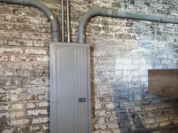 Industrial electrical panel with gray conduits mounted on a brick wall, showcasing durable Cordura RE fabric application in industrial wiring systems.