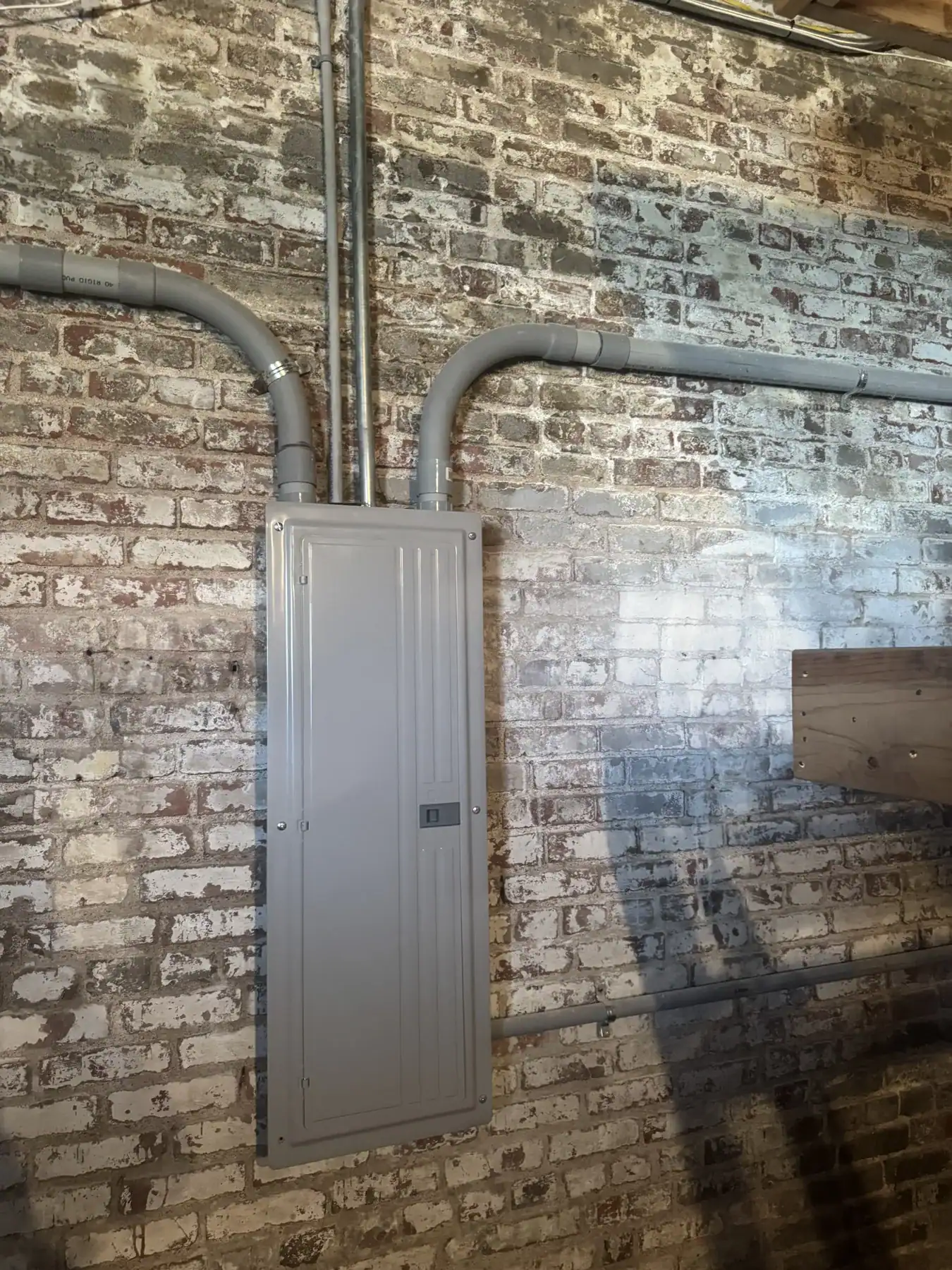 Industrial electrical panel with gray conduits mounted on a brick wall, showcasing durable Cordura RE fabric application in industrial wiring systems.